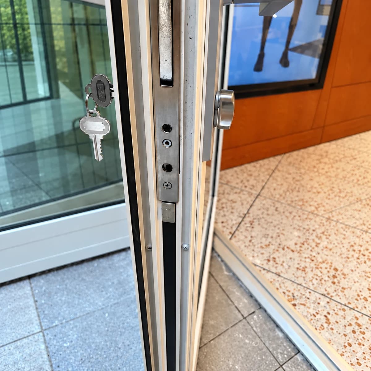 Open aluminum/glazed entry door edge with lock faceplate and two keys at the left