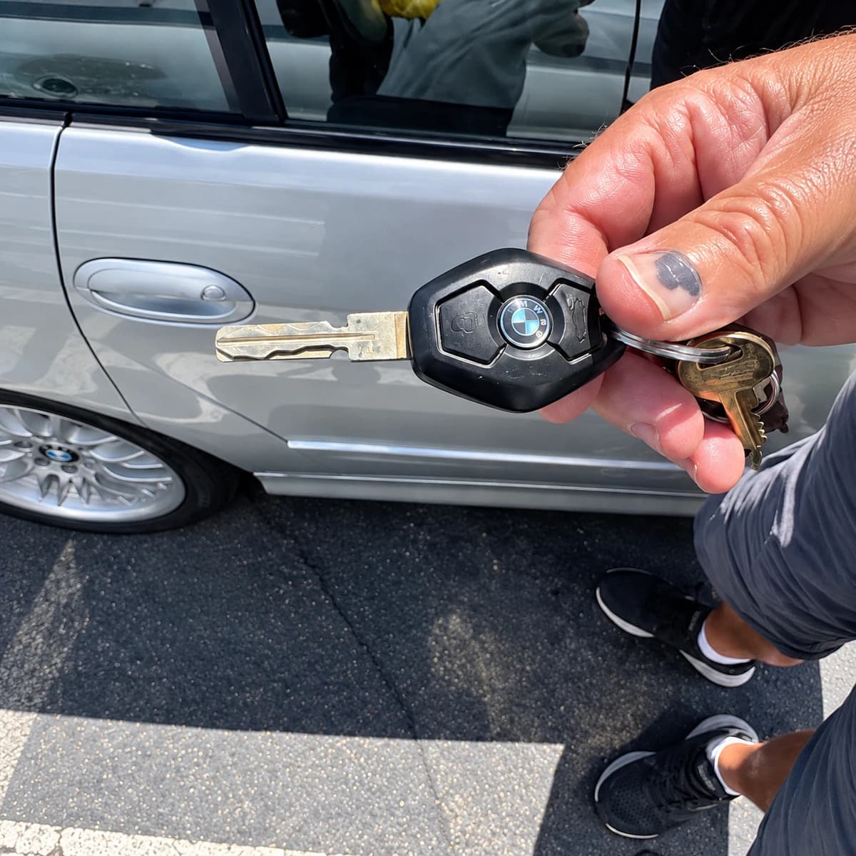 Metal vehicle key with a black polygonal head held beside a silver vehicle.