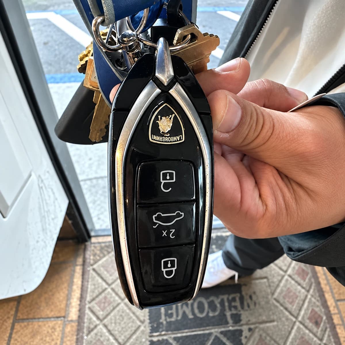 Black-and-chrome three-button vehicle key fob held with a keyring.
