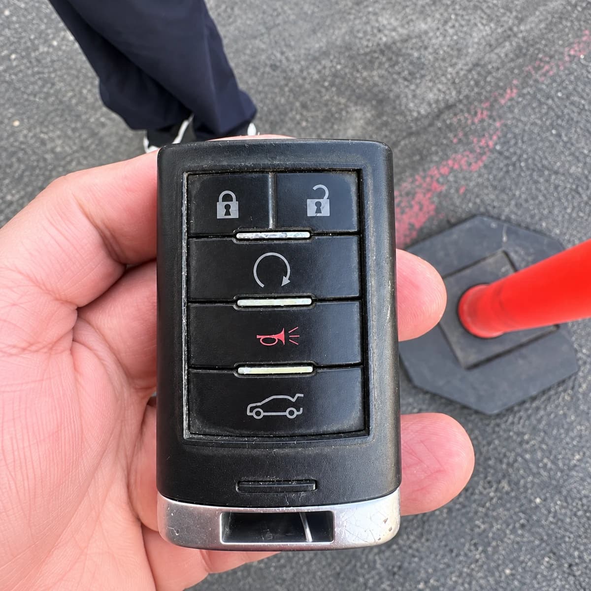 Rectangular five-button vehicle remote held in a hand.